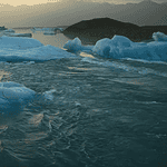 New doc ‘Time and Water’ at OKCMOA a staggering eulogy for nature Icebergs floating in a calm glacial lagoon at sunset with distant mountains in the background, reflecting on the water.