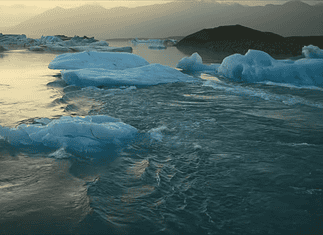 New doc ‘Time and Water’ at OKCMOA a staggering eulogy for nature Icebergs floating in a calm glacial lagoon at sunset with distant mountains in the background, reflecting on the water.