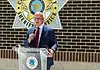 Weaver named new Cleveland Co. sheriff; no FBI investigation expected Man in a navy suit and red tie speaks into a handheld microphone at a clear podium bearing a circular seal, with a sheriff’s office emblem on a brick wall behind him.
