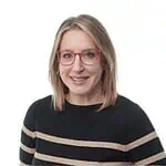 Portrait of a smiling woman with shoulder-length blonde hair and red-framed glasses, wearing a black sweater with beige stripes