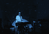 Person seated at a keyboard in a dim, blue-lit room with green star projector specks on the walls and floor.