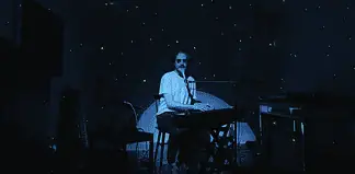 Person seated at a keyboard in a dim, blue-lit room with green star projector specks on the walls and floor.