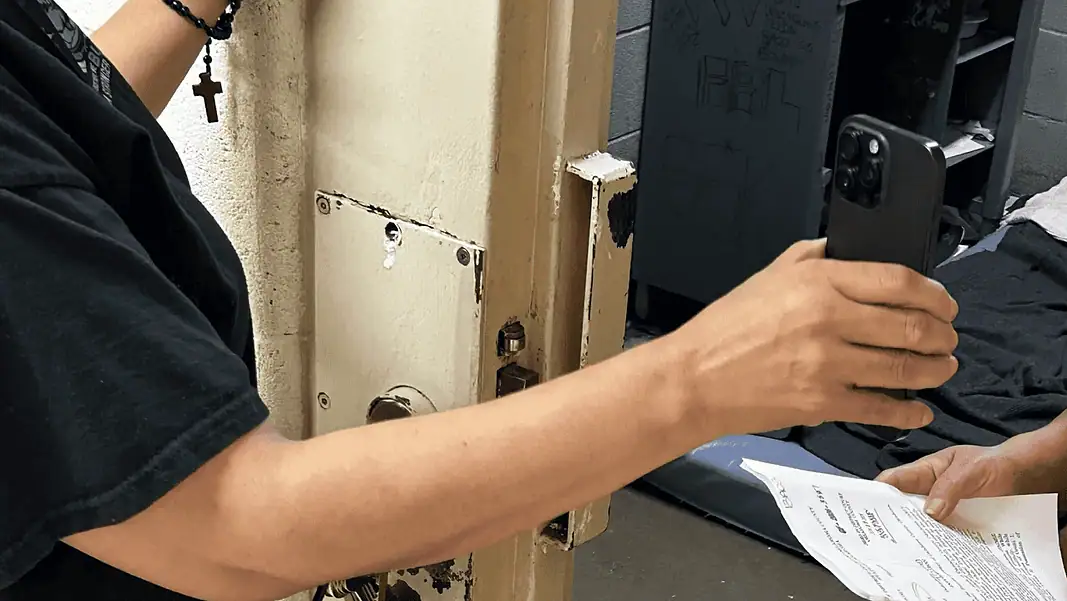 Frontier 1 Person in a black shirt holds a smartphone to photograph printed papers being handed to them near a rusty metal door.