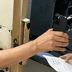 Oklahoma County bail hearings don’t meet constitutional standards, attorneys say Person in a black shirt holds a smartphone to photograph printed papers being handed to them near a rusty metal door.