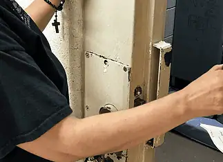 Oklahoma County bail hearings don’t meet constitutional standards, attorneys say Person in a black shirt holds a smartphone to photograph printed papers being handed to them near a rusty metal door.