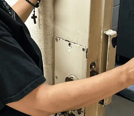 Oklahoma County bail hearings don’t meet constitutional standards, attorneys say Person in a black shirt holds a smartphone to photograph printed papers being handed to them near a rusty metal door.