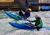 Riversport OKC scores big hosting World Championships ahead of Olympics Two kayakers wearing helmets navigate whitewater rapids in blue kayaks, paddling aggressively through churning water.