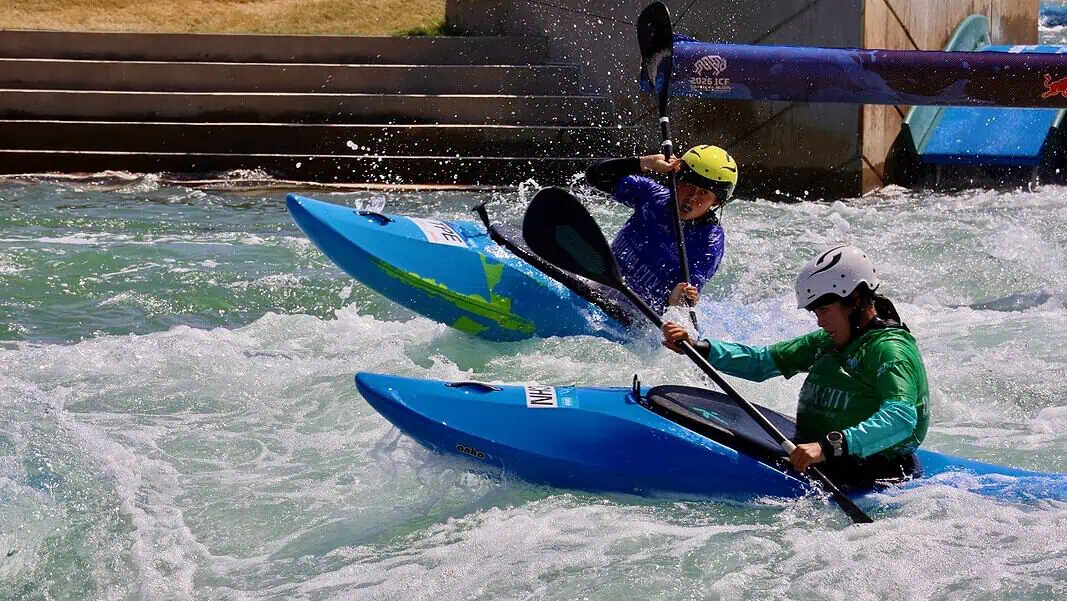 IMG_2199 Two kayakers wearing helmets navigate whitewater rapids in blue kayaks, paddling aggressively through churning water.