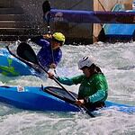Riversport OKC scores big hosting World Championships ahead of Olympics Two kayakers wearing helmets navigate whitewater rapids in blue kayaks, paddling aggressively through churning water.