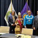 PRESS RELEASE: Five Tribes call for oversight of prediction markets Six people in formal attire stand on a stage with colorful banners and flags behind them, posing for a group photo.