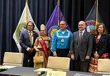 PRESS RELEASE: Five Tribes call for oversight of prediction markets Six people in formal attire stand on a stage with colorful banners and flags behind them, posing for a group photo.
