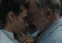 Hypnotic, unsettling ‘Night Nurse’ a piercing portrait of sociopathy Young woman and an older man press foreheads together in a tender, intimate moment beside a wall.