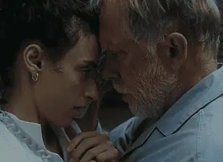 Hypnotic, unsettling ‘Night Nurse’ a piercing portrait of sociopathy Young woman and an older man press foreheads together in a tender, intimate moment beside a wall.