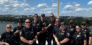 Group of police officers posing for a photo on a boat or dock with the Washington Monument in the background along the Potomac River