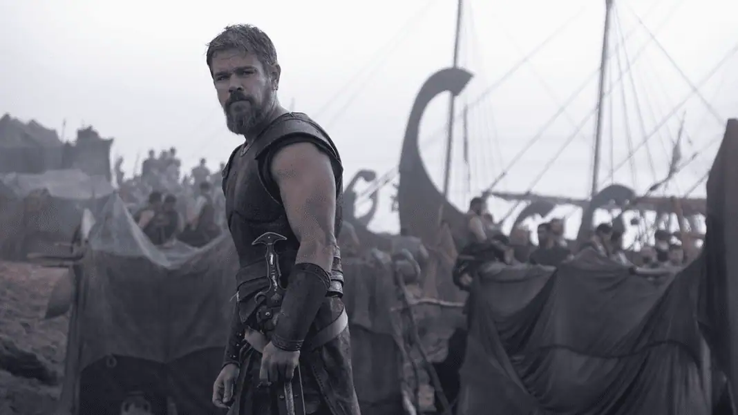 Odyssey 10 Bearded warrior in dark armor stands at the edge of a tents-filled camp with ships and masts in the misty background.