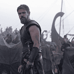 Nolan’s ‘Odyssey’ an epic emotional outburst of present politics, pains Bearded warrior in dark armor stands at the edge of a tents-filled camp with ships and masts in the misty background.