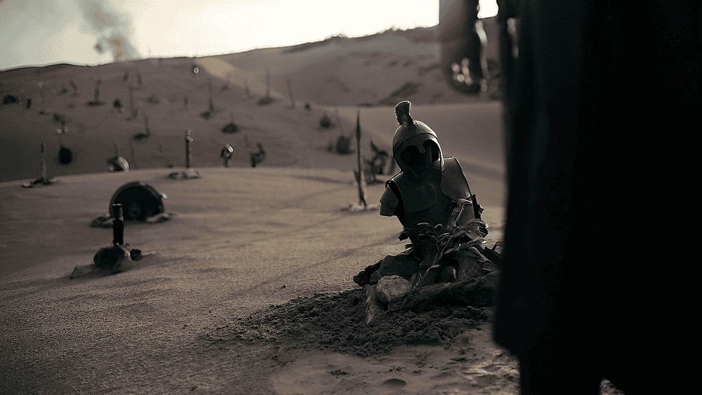 Dusty desert landscape with scattered armor pieces and a blue helmet perched on rocks in the sand.