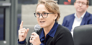 Woman with glasses speaking into a microphone during a panel discussion in a conference setting.