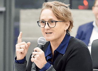 Paula Lewis resigns from Oklahoma City school board after historic tenure Woman with glasses speaking into a microphone during a panel discussion in a conference setting.
