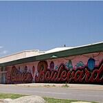 PRESS RELEASE: Residents invited to help shape the future of the Classen Corridor Clear blue sky over a street with a long mural spelling 'Boardwalk' along a pink-walled building.