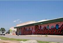 Clear blue sky over a street with a long mural spelling 'Boardwalk' along a pink-walled building.