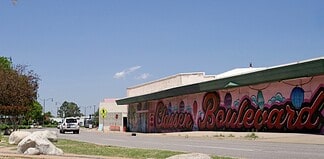 Clear blue sky over a street with a long mural spelling 'Boardwalk' along a pink-walled building.