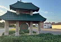 Police host public discussion over homelessness, crime in Asian District Pagoda-style shelter with a teal, wavy roof over a circular 'Asian' sign on a grassy median by the road.
