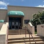City forced to euthanize 250 birds seized in June drug bust Entrance to a beige building with green curved awnings, concrete stairs, and metal railings under a blue sky.