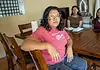 People deported by ICE leave behind families, lasting trauma Woman in a pink shirt sits at a wooden dining table, facing the camera, with two others blurred in the background in a home setting.