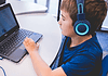 An all-AI private school with no teachers is set to open in Edmond Child wearing blue headphones typing on a Dell laptop at a white table in a classroom or study area