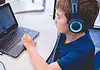 An all-AI private school with no teachers is set to open in Edmond Child wearing blue headphones typing on a Dell laptop at a white table in a classroom or study area