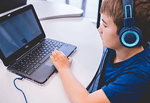 An all-AI private school with no teachers is set to open in Edmond Child wearing blue headphones typing on a Dell laptop at a white table in a classroom or study area