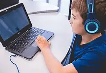 An all-AI private school with no teachers is set to open in Edmond Child wearing blue headphones typing on a Dell laptop at a white table in a classroom or study area
