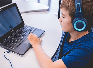 An all-AI private school with no teachers is set to open in Edmond Child wearing blue headphones typing on a Dell laptop at a white table in a classroom or study area