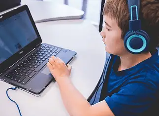 An all-AI private school with no teachers is set to open in Edmond Child wearing blue headphones typing on a Dell laptop at a white table in a classroom or study area