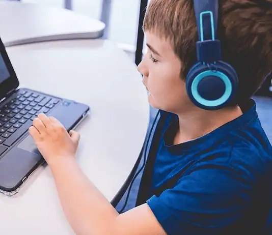 An all-AI private school with no teachers is set to open in Edmond Child wearing blue headphones typing on a Dell laptop at a white table in a classroom or study area