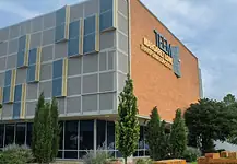 Poor defendants often blocked from OK County pretrial release program Modern brick building with a grey panel facade and blue-yellow decorative panels; a sign on the brick wall reads Transformation Center, with glass windows and trees in front.