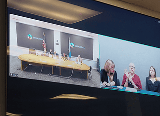 State executes longtime death row inmate convicted in OKC murder Split-screen video conference of a government meeting: left panel shows officials at a long table with flags in an Oklahoma setting; right panel shows three women, one signing, at a different location.