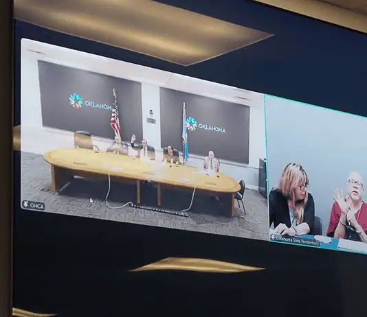 State executes longtime death row inmate convicted in OKC murder Split-screen video conference of a government meeting: left panel shows officials at a long table with flags in an Oklahoma setting; right panel shows three women, one signing, at a different location.