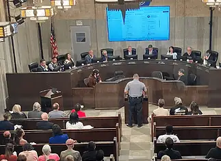 City Council votes to renew contract for controversial Flock cameras Uniformed officer at the podium addressing a city council chamber full of attendees at a curved dais.