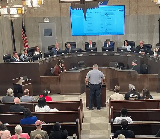 City Council votes to renew contract for controversial Flock cameras Uniformed officer at the podium addressing a city council chamber full of attendees at a curved dais.