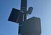 Streetlight pole with a solar panel, security camera, and large control box against a blue sky.