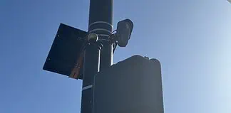 Streetlight pole with a solar panel, security camera, and large control box against a blue sky.
