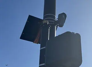 City to vote on sweeping ‘guardrails’ for Flock cameras as OKCPD continues use Streetlight pole with a solar panel, security camera, and large control box against a blue sky.