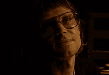 OFX hosting hyper-modern horror pic from indie-rock hero Woman wearing oversized glasses in a dim, sepia-toned room, looking upward with a soft smile under warm lighting.