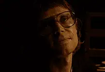 OFX hosting hyper-modern horror pic from indie-rock hero Woman wearing oversized glasses in a dim, sepia-toned room, looking upward with a soft smile under warm lighting.