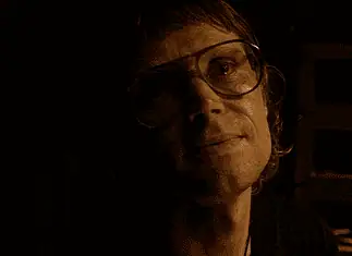OFX hosting hyper-modern horror pic from indie-rock hero Woman wearing oversized glasses in a dim, sepia-toned room, looking upward with a soft smile under warm lighting.
