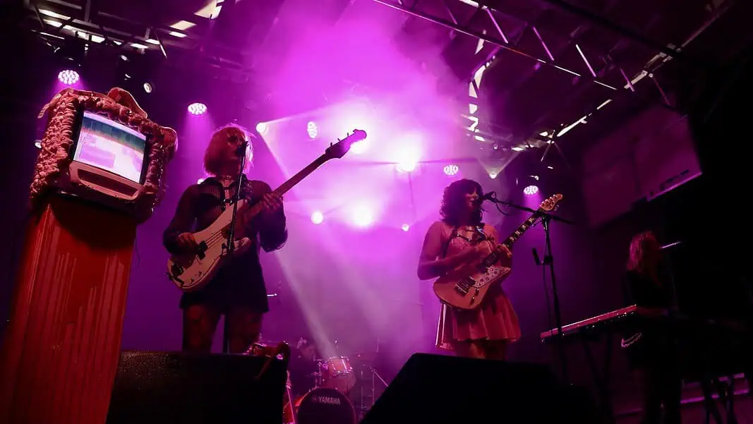 stepmom (photo by Zoe Elrod for OKC Free Press) Band performing on a lit stage with purple lights; two guitarists and a keyboard player, drum kit in back, vintage TV on a red pedestal to the left.