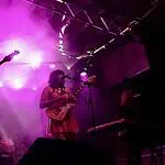 Catch these scene-leading locals opening for can’t-miss nationals across OKC Band performing on a lit stage with purple lights; two guitarists and a keyboard player, drum kit in back, vintage TV on a red pedestal to the left.