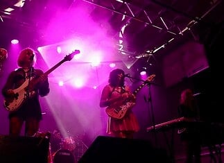 Catch these scene-leading locals opening for can’t-miss nationals across OKC Band performing on a lit stage with purple lights; two guitarists and a keyboard player, drum kit in back, vintage TV on a red pedestal to the left.